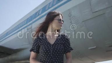 肖像可爱的年轻自信的黑发女孩戴着太阳镜站在<strong>大飞机</strong>前面。 夏天。 快乐